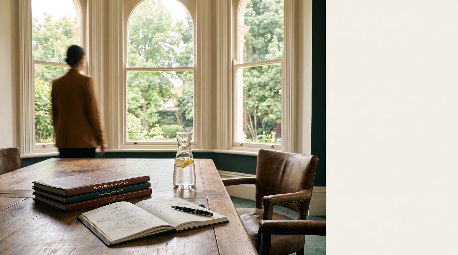 A refined Australian meeting library with impact reports, theory-of-change notes, a carafe of lemon water, and a professional silhouette by tall windows.